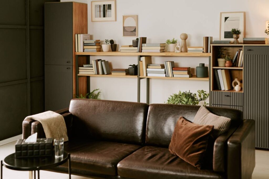 Modern living room interior featuring an empty brown leather sofa positioned in front of bookshelves