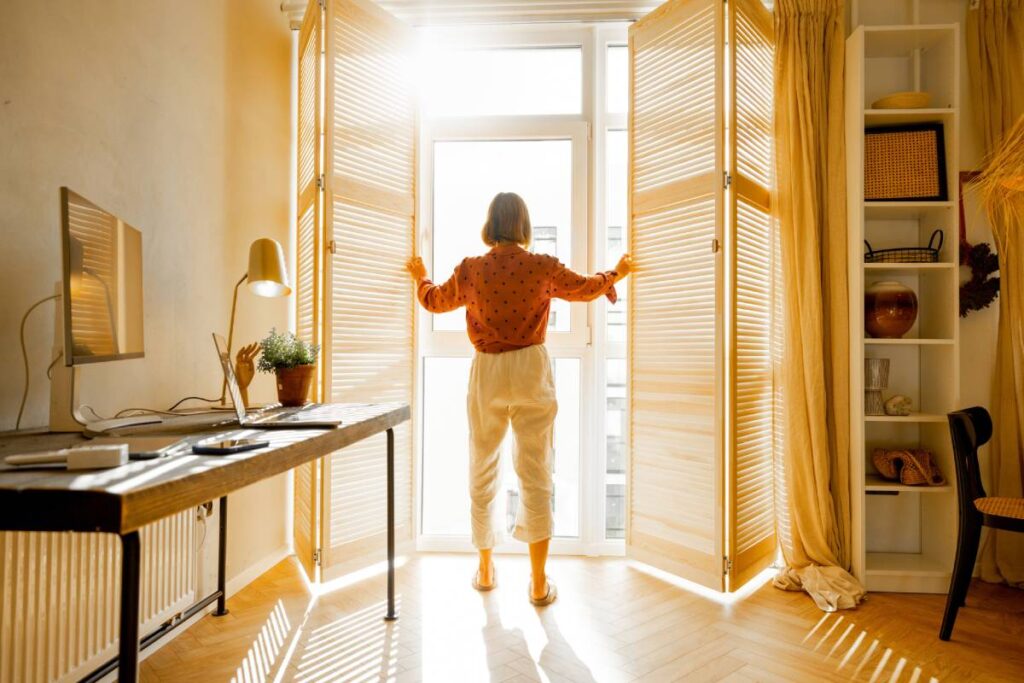 Person opening window shutters, letting the sun inside a cozy apartment in beige tones